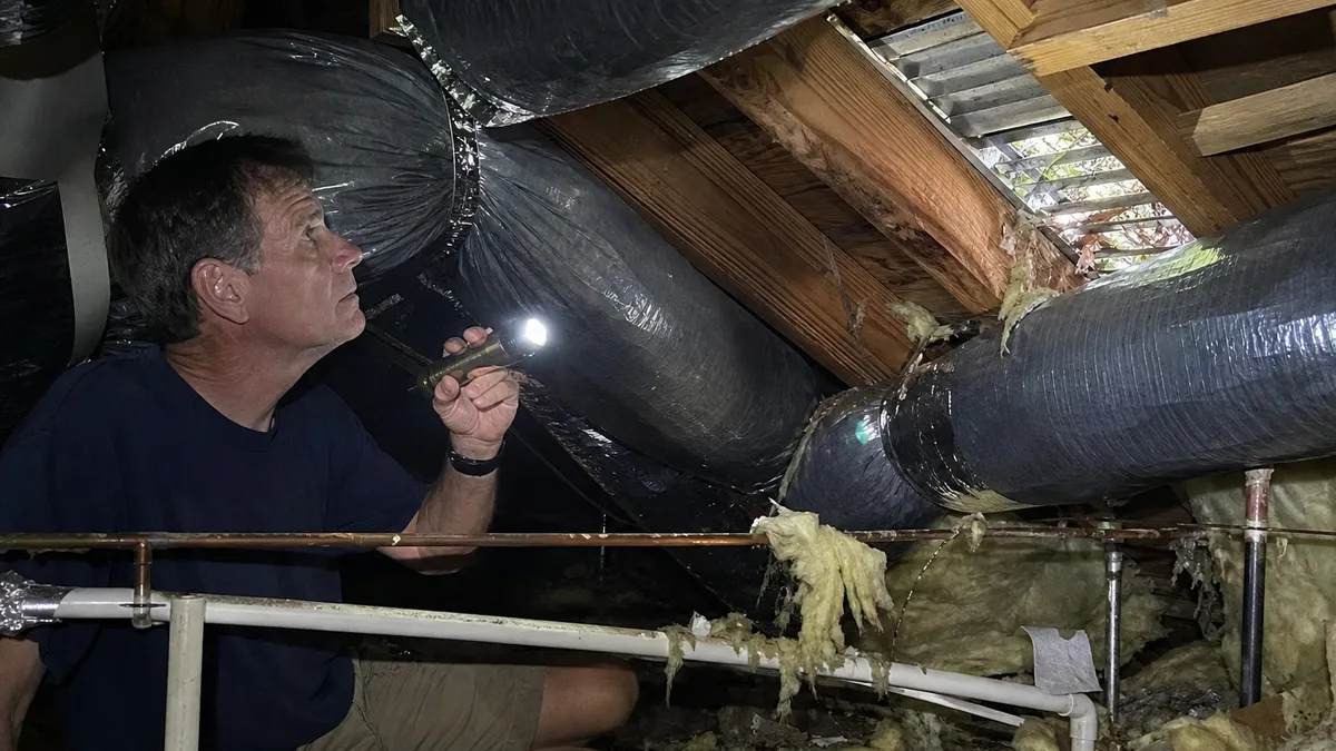 Florida homeowner with flashlight inspecting attic ductwork after hurricane